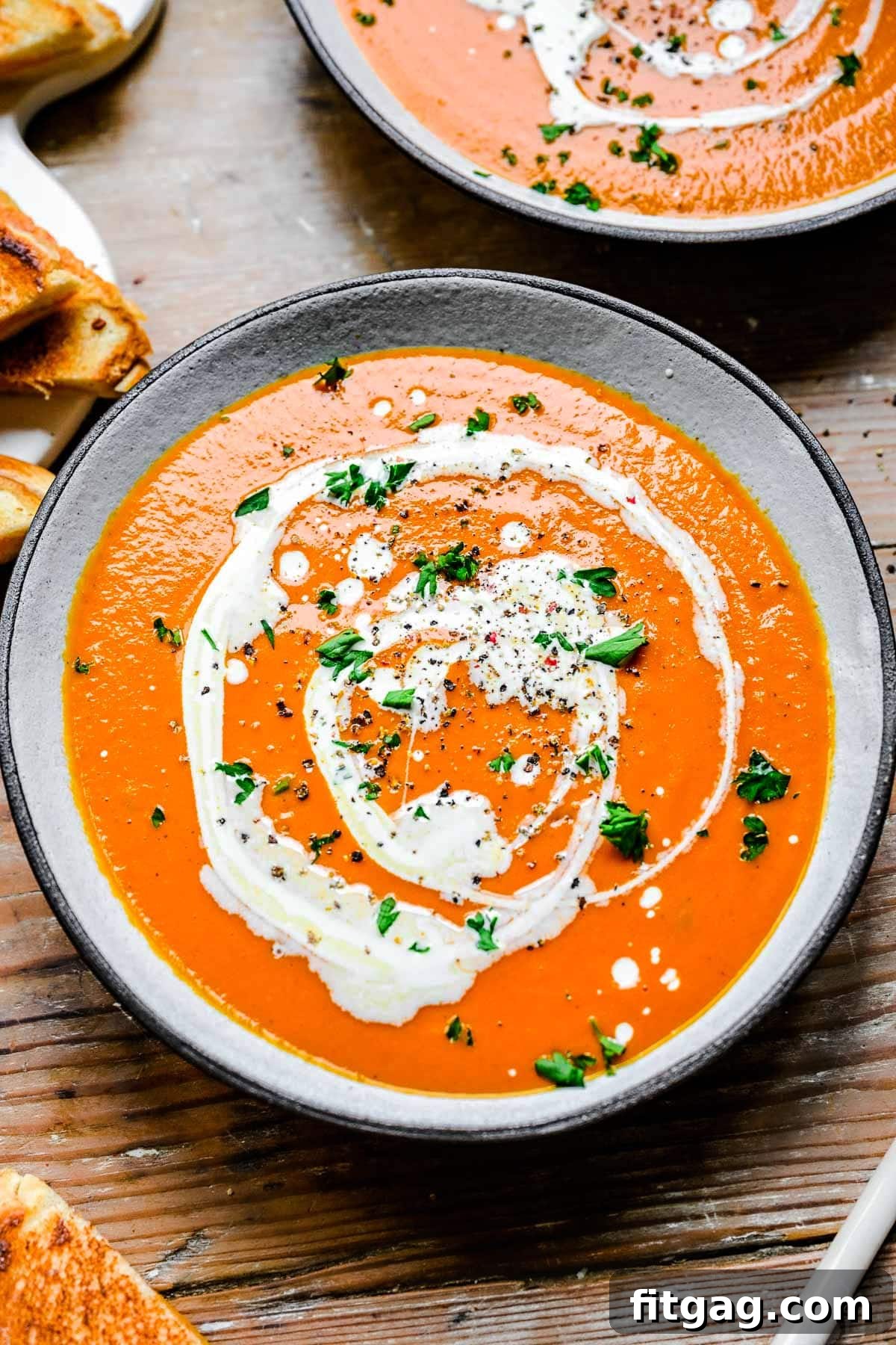 A steaming bowl of Instant Pot Tomato Soup, drizzled with heavy cream and garnished with fresh chopped basil.