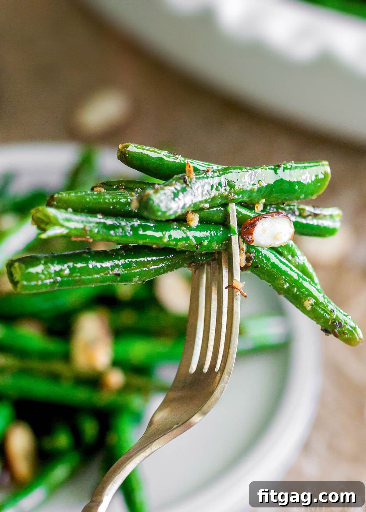 Forkful of garlic green beans held over a white plate, showcasing the vibrant green and golden brown accents.