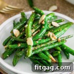 Small round white plate with a serving of garlic green beans on it.