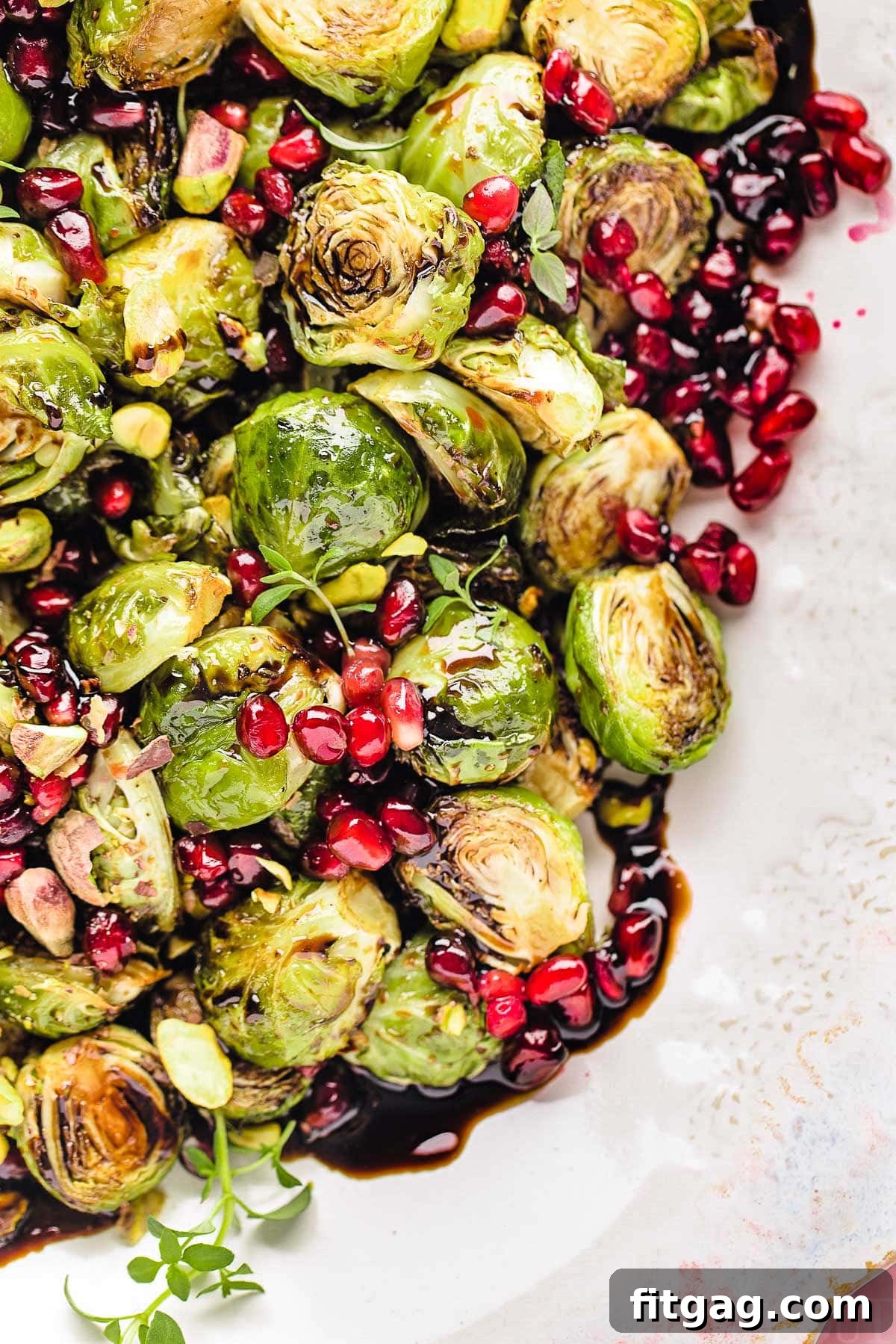 Caramelized Roasted Brussels Sprouts 2 Top down view of roasted brussels sprouts on a pink and white serving dish. the sprouts are topped with pomegranate seeds and thyme along with a balsamic glaze.