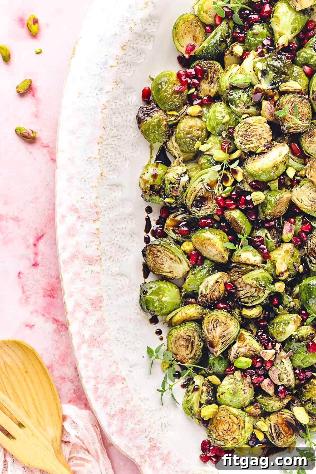 Caramelized Roasted Brussels Sprouts 4 top down view of roasted brussels sprouts on a large white and pink platter. Pomegranate seeds and pistachios garnish the gorgeous dish.