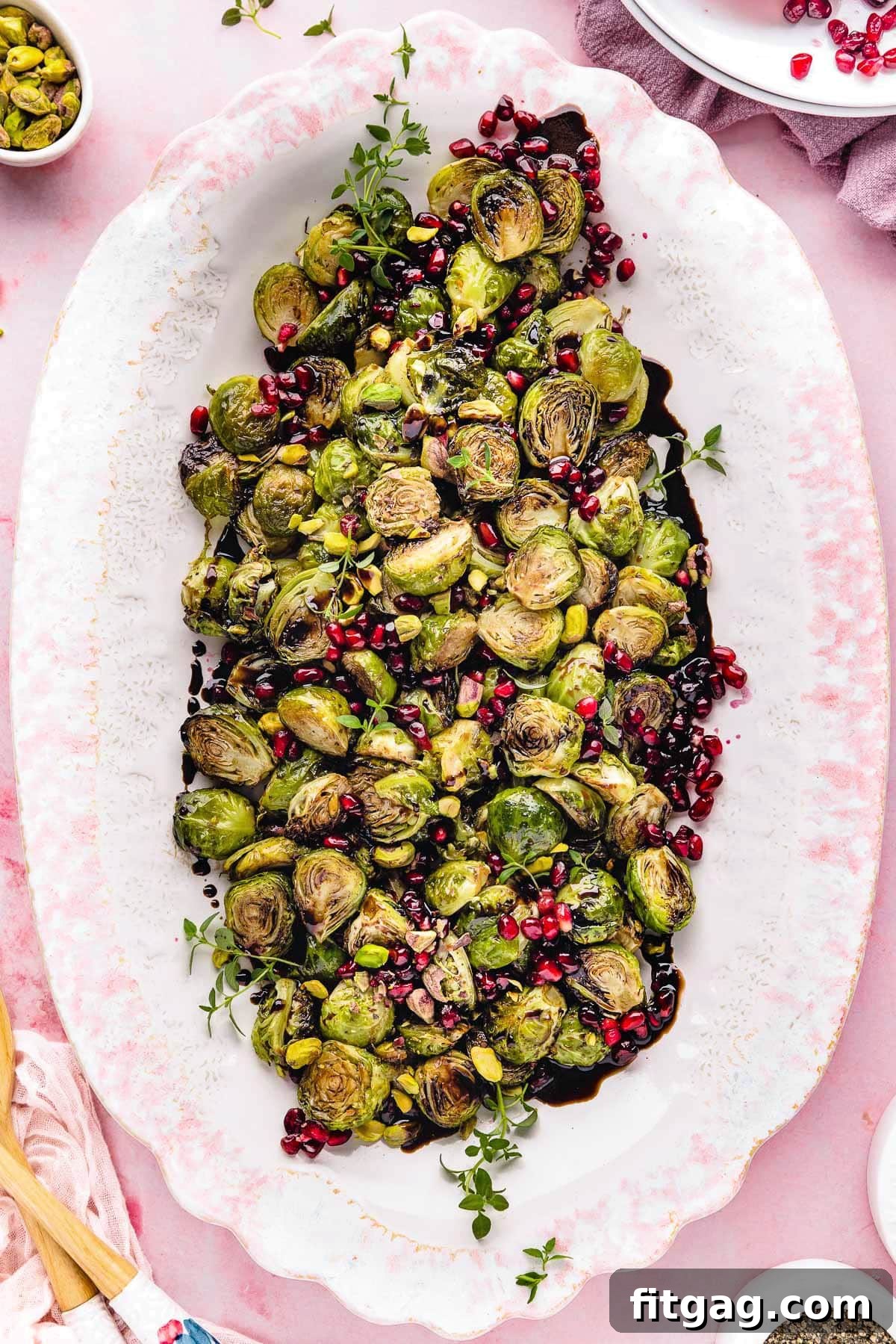 Caramelized Roasted Brussels Sprouts 6 top down view of roasted brussels sprouts on a large white and pink platter. Pomegranate seeds and pistachios garnish the gorgeous dish.