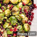 Top down view of roasted brussels sprouts on a pink and white serving dish. the sprouts are topped with pomegranate seeds and thyme along with a balsamic glaze.