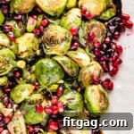 Caramelized Roasted Brussels Sprouts 8 Top down view of roasted brussels sprouts on a pink and white serving dish. the sprouts are topped with pomegranate seeds and thyme along with a balsamic glaze.