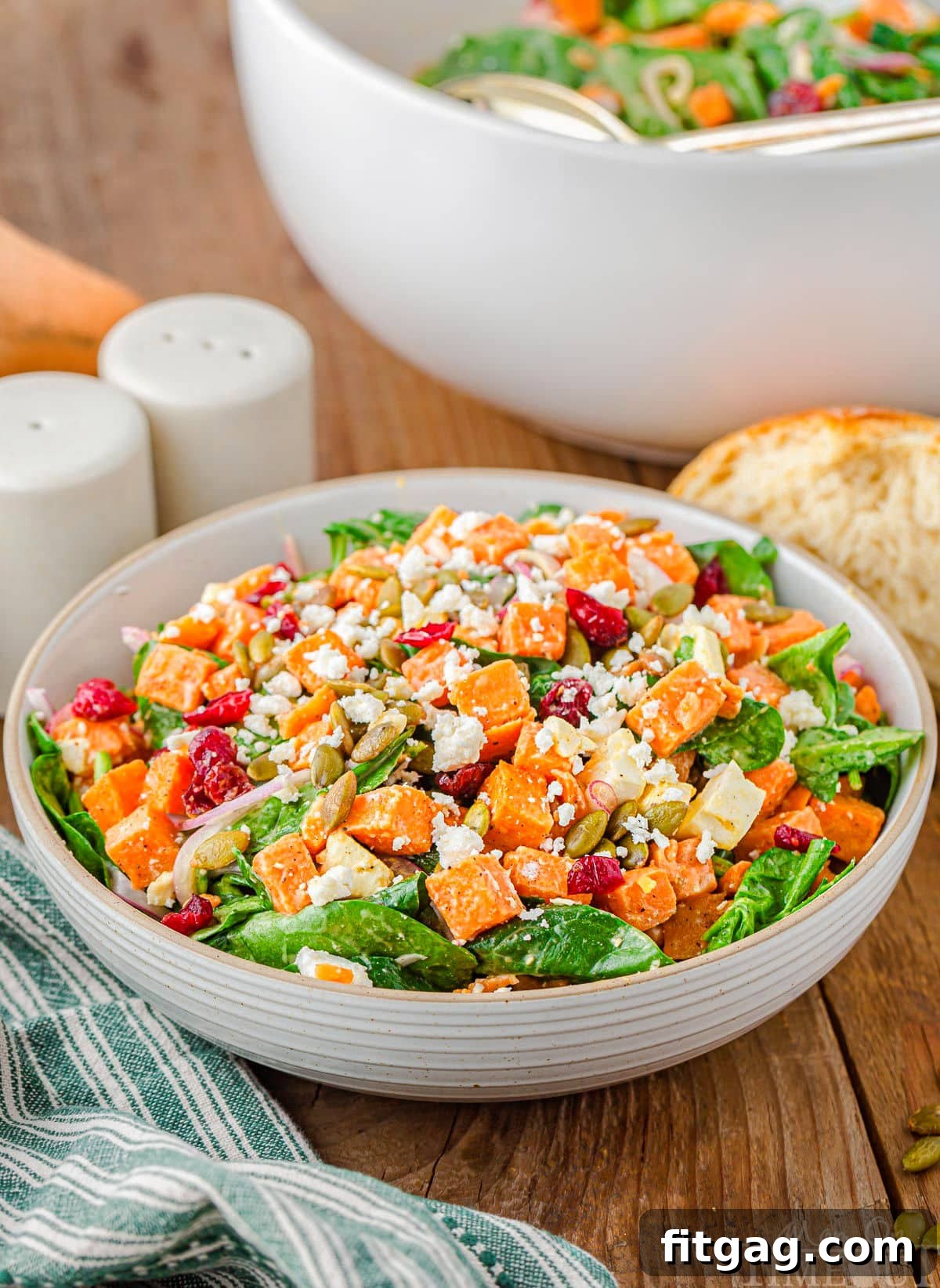 A large, inviting bowl of sweet potato salad, richly topped with roasted sweet potato cubes, dried cranberries, pepitas, and crumbled feta cheese, ready to be served.