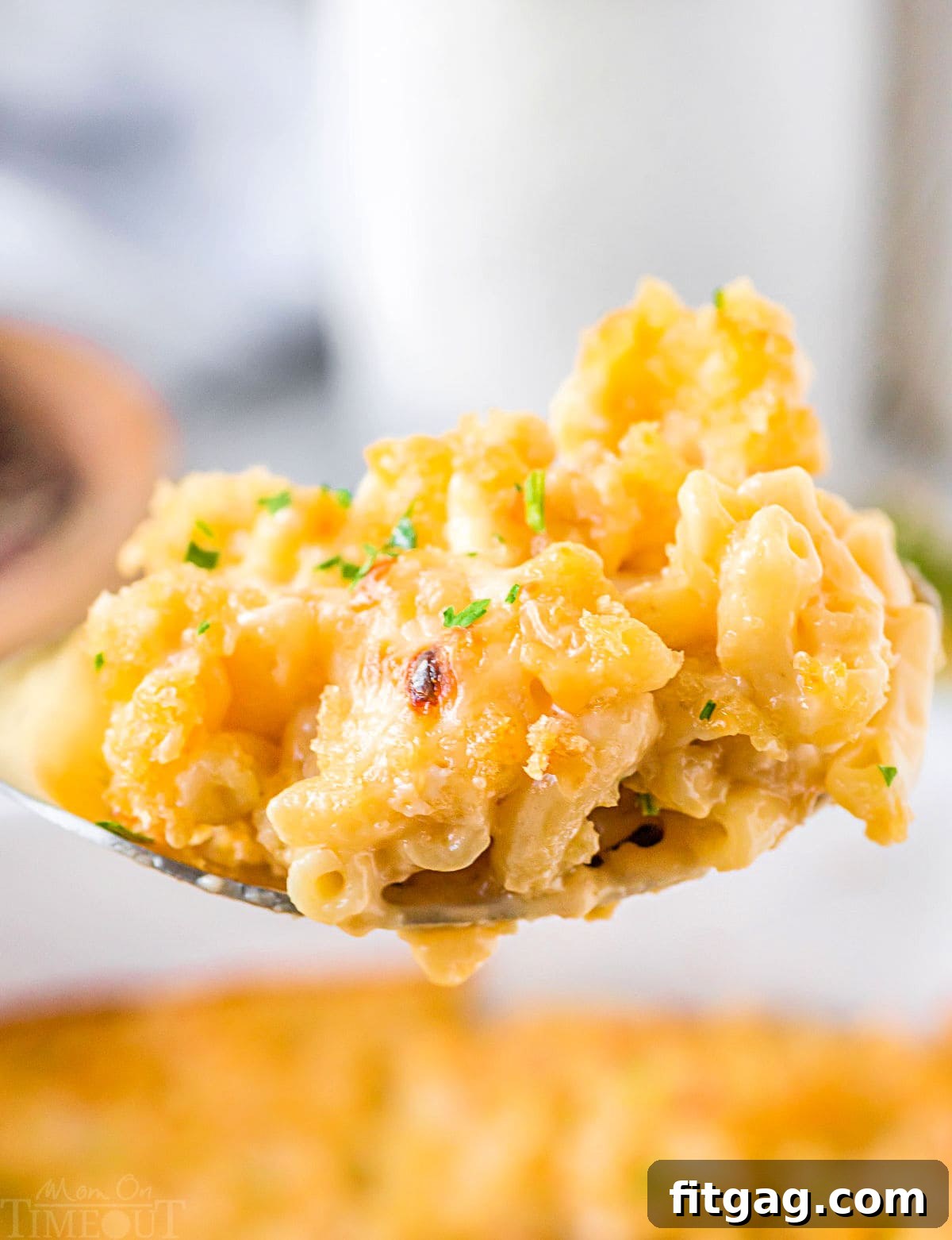 Liquid Gold Mac 6 large spoon full of creamy velveeta mac and cheese held above the casserole dish.