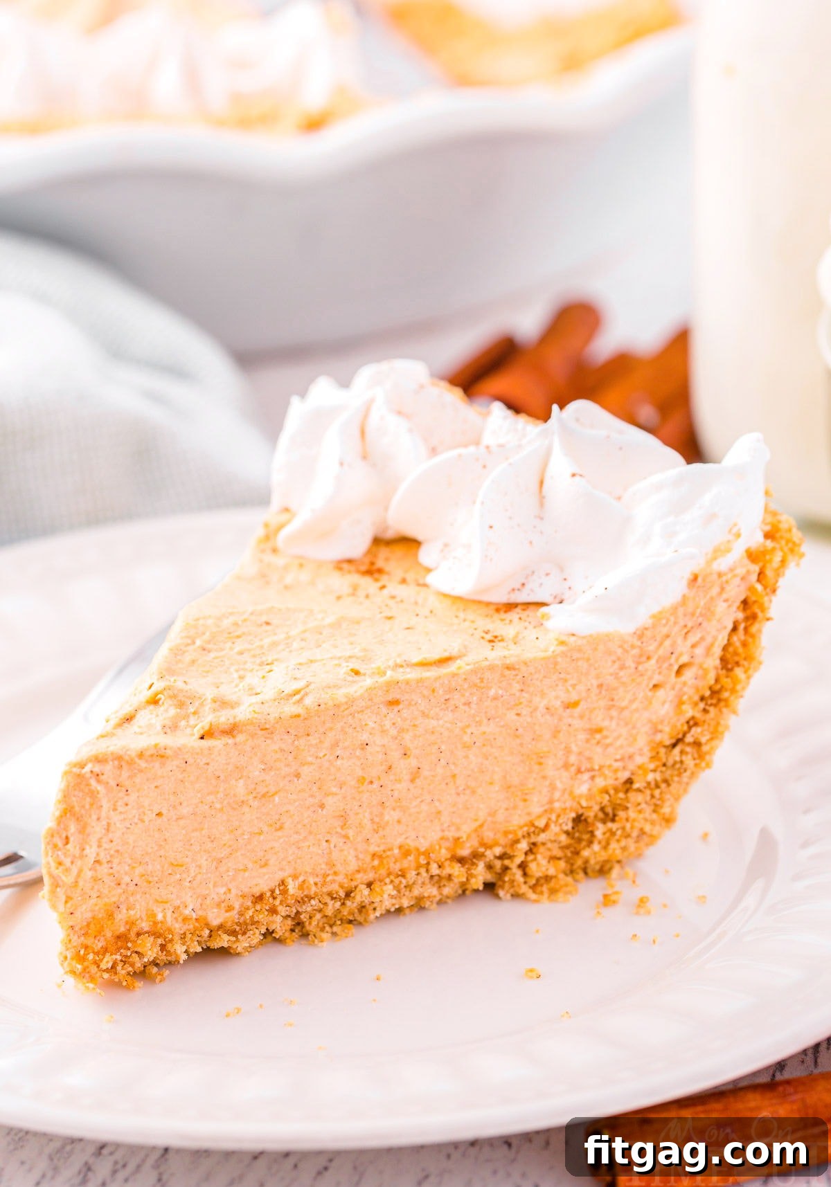 Effortless Pumpkin Pie 2 A perfectly portioned slice of no-bake pumpkin pie, elegantly presented on a white plate and crowned with a generous swirl of fresh whipped cream, ready to be enjoyed.