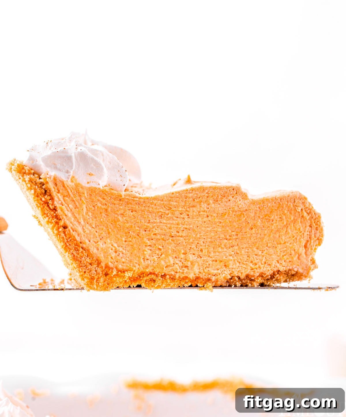 Effortless Pumpkin Pie 3 A delicious slice of no-bake pumpkin pie, carefully lifted above the pie plate, showcasing its smooth, creamy layers and golden crust.