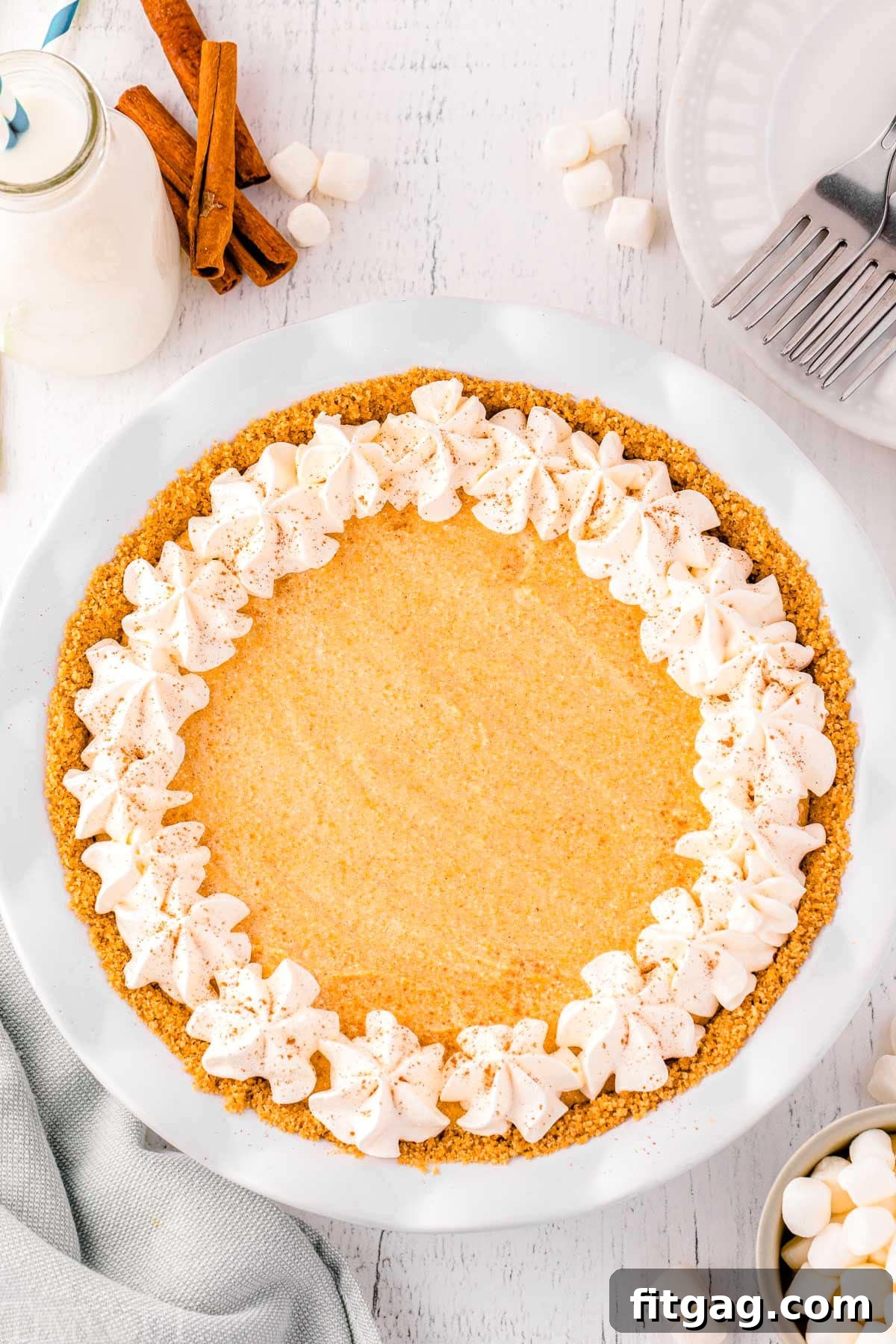 Effortless Pumpkin Pie 4 A stunning top-down view of a whole no-bake pumpkin pie, perfectly set and garnished, resting on a sophisticated marble surface, flanked by elegant cinnamon sticks, ready for its close-up.