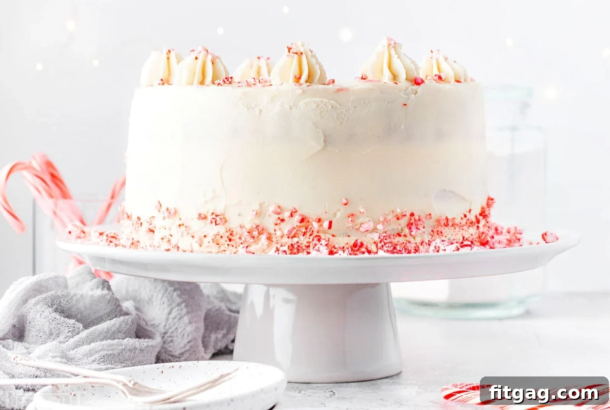 Frosted Peppermint Indulgence 4 A meticulously frosted Peppermint Cake stands tall on a white cake stand, adorned with a delicate scattering of crushed candy canes around its base, creating an irresistible holiday vision.