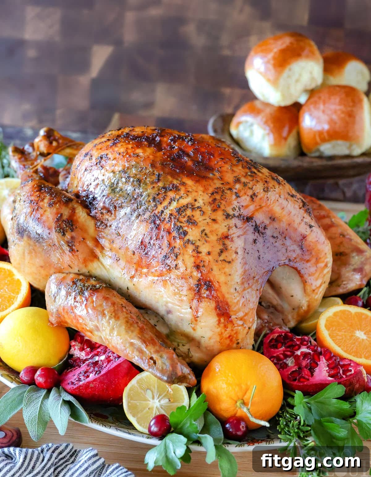 Unlock the Juiciest Thanksgiving Turkey 2 How To Cook A Turkey recipe with the whole roast turkey on a serving platter garnished with fresh fruit and herbs. Dinner rolls can be seen in the background.
