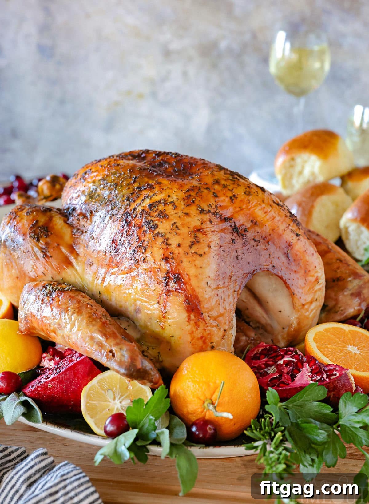 Unlock the Juiciest Thanksgiving Turkey 13 A perfect turkey recipe on a large serving platter roasted until golden brown and surround by citrus, herbs and cranberries. Dinner rolls can be seen in the background.