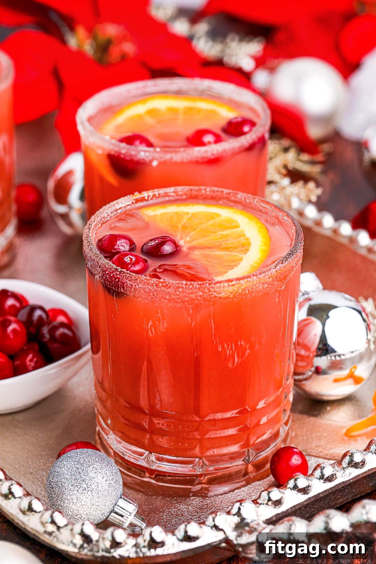 Holiday Spirit Sips 2 two Christmas cocktails on a silver serving platter garnished with fresh cranberries and orange slices, a perfect holiday drink.