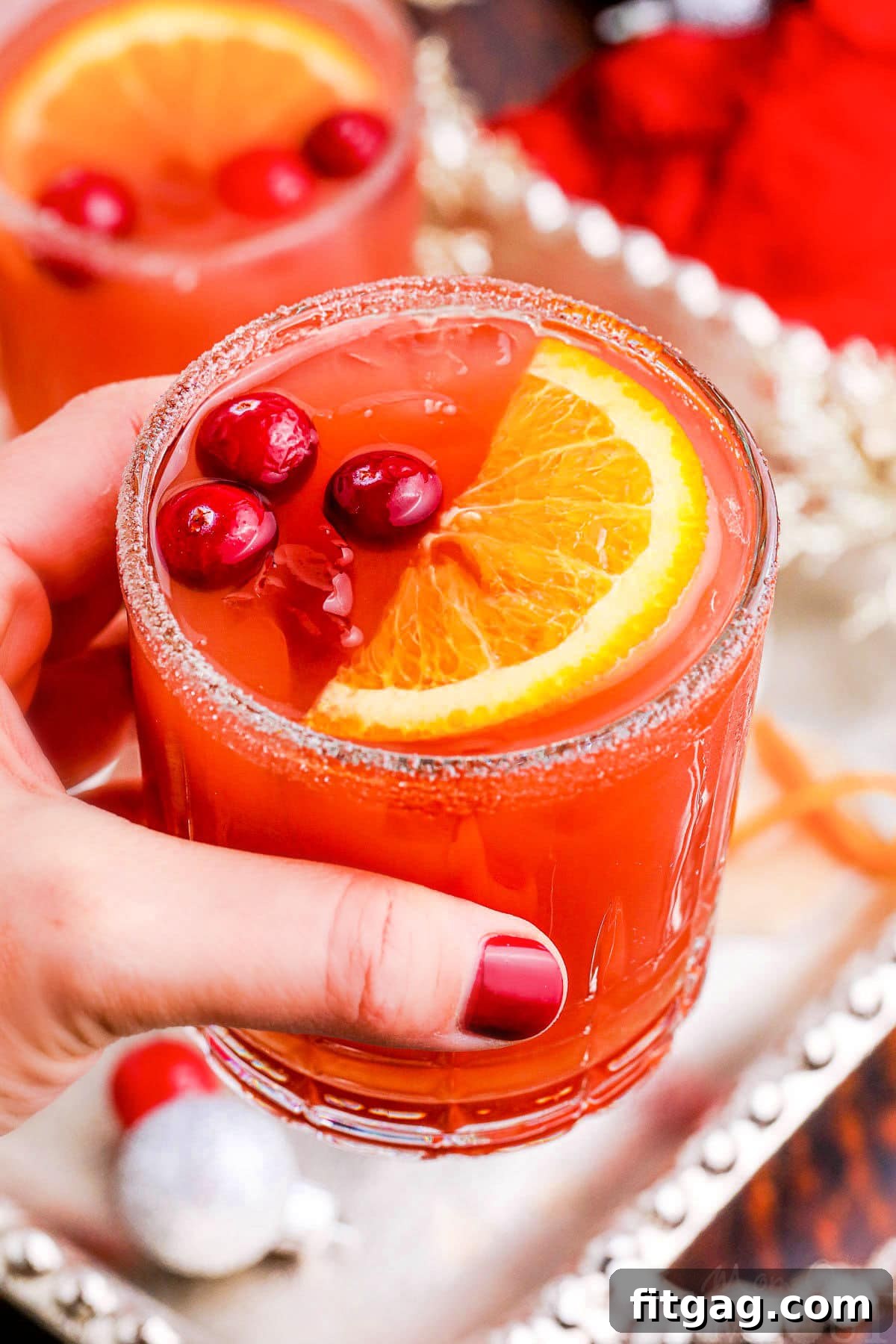 Holiday Spirit Sips 3 A hand holding a glass of Christmas cocktail, made with a vibrant mix of cranberry juice, orange juice, and amaretto.