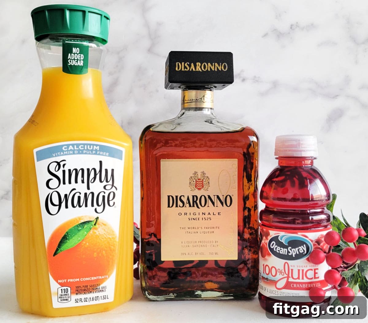 Holiday Spirit Sips 4 Orange juice, amaretto liqueur, and cranberry juice sit on a white surface, perfectly lined up and ready to be used in the Christmas cocktail recipe.