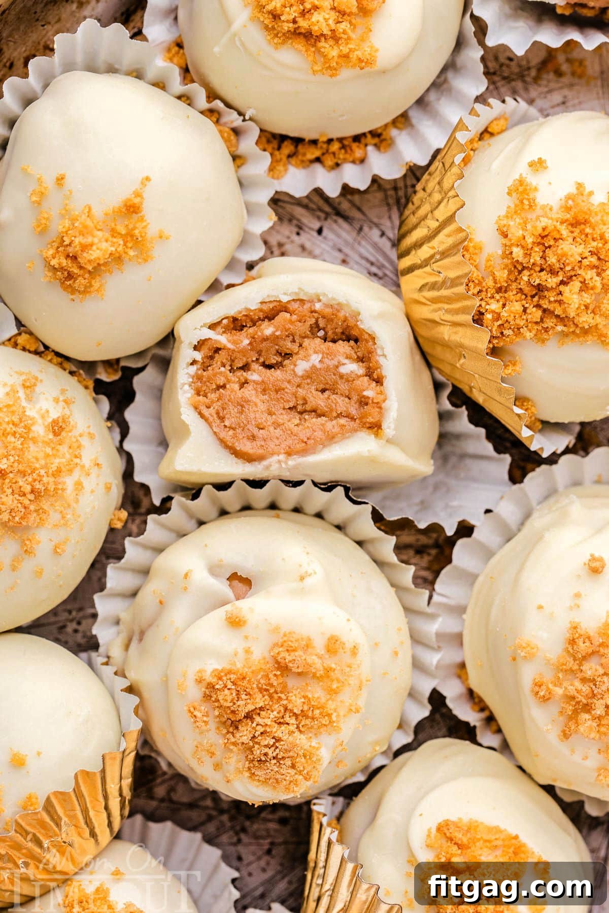 Delightful gingerbread truffles coated in white chocolate and sprinkled with gingersnap cookie crumbles, presented in elegant white paper cups. One truffle has a tempting bite taken out of it.
