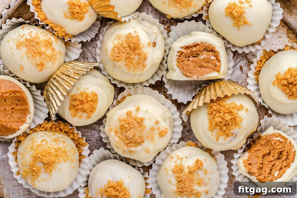 A top-down view of easy gingerbread truffles in white paper cups, arranged on a silver parchment tray. Several truffles show a cross-section, revealing their creamy interior.