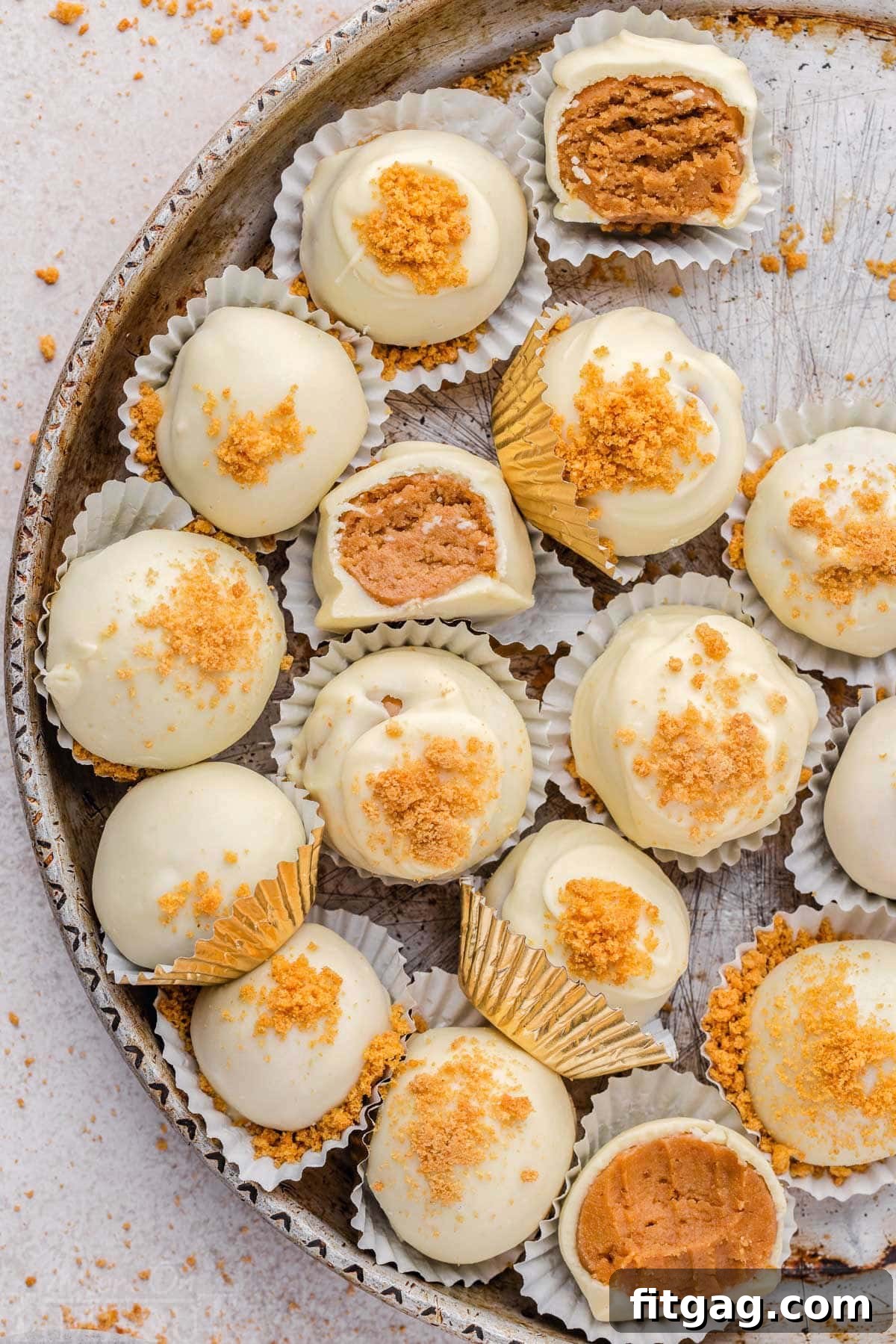 Gingerbread truffles in white paper cups, coated in white chocolate and sprinkled with gingersnap crumbles. Three of the truffles have been partially eaten, showing the soft interior.