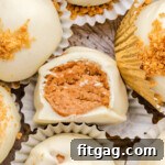 Gingerbread truffles in white paper cups with gingersnap cookies crumbles sprinkles on top of the white chocolate coating. one truffle has a bite out of it.