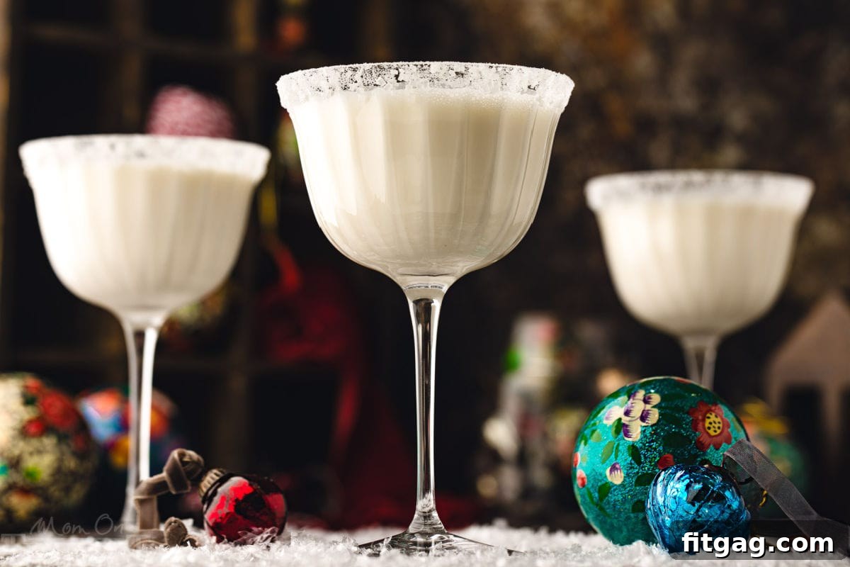 Three white chocolate martinis in tall glasses, beautifully dusted with powdered sugar for a snowy effect, artfully placed on a pristine snowy surface with scattered glass ornaments, creating a stunning winter display.