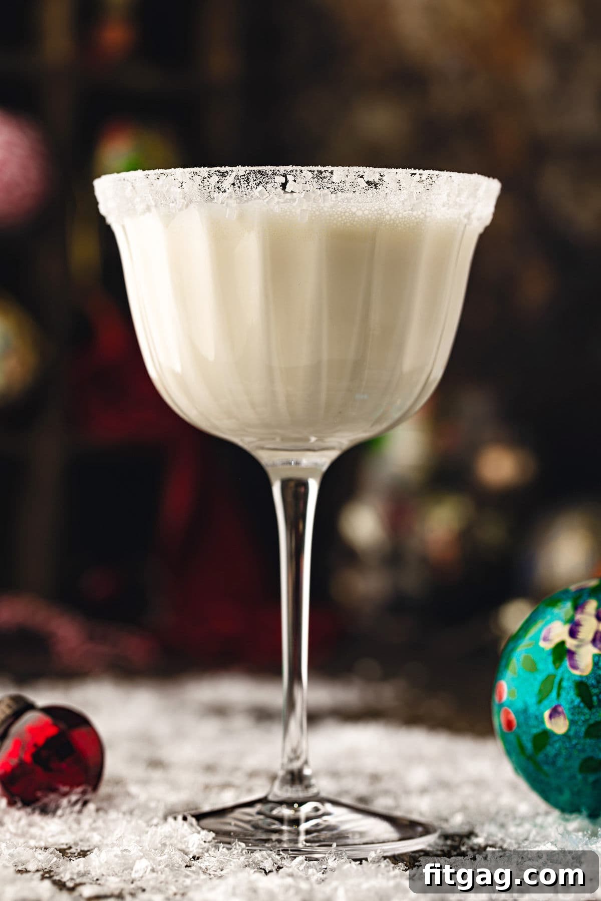 A pristine white chocolate martini cocktail, elegantly served in a tall glass and dusted with powdered sugar for a snowy effect. The drink is placed on a festive snowy surface, surrounded by delicate glass ornaments, creating a charming holiday scene.