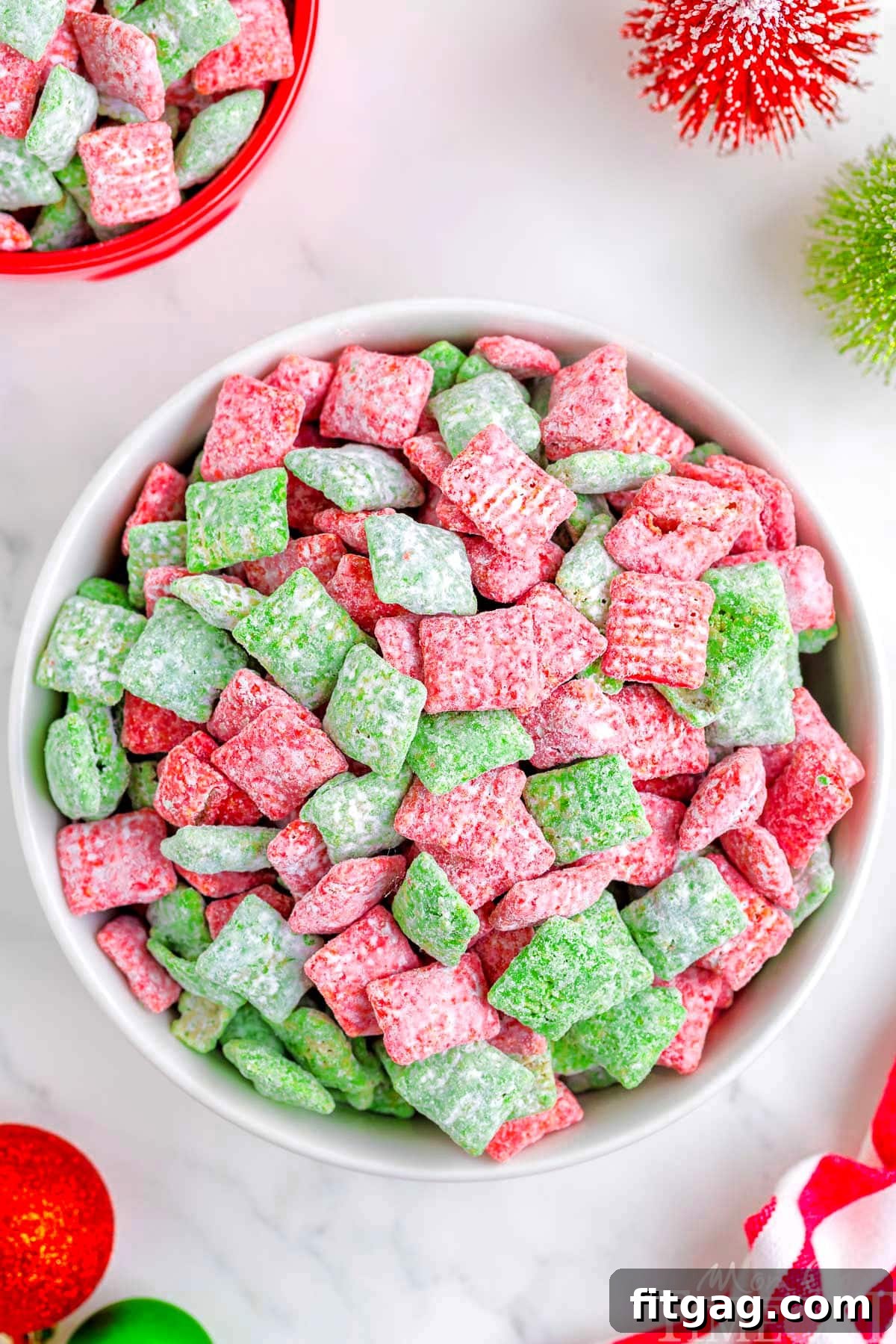 Holiday Crunch Mix 2 Top-down view of a large white bowl brimming with festive Christmas Puppy Chow, showcasing a vibrant mix of red and green muddy buddies dusted with powdered sugar, ready for holiday celebrations.