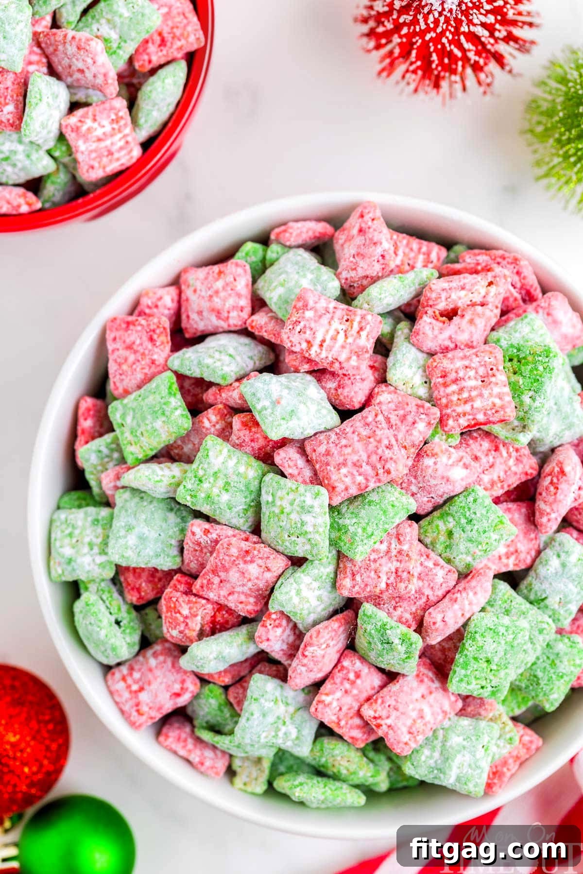 Holiday Crunch Mix 6 A large white bowl generously filled with vibrant Christmas Muddy Buddies, featuring red and green coated Chex cereal, perfectly arranged for a festive display.