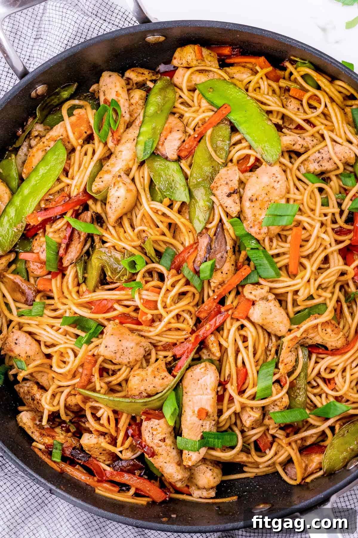 Top-down view of chicken lo mein served in a dark skillet, showcasing an abundance of colorful vegetables, succulent chicken pieces, and perfectly intertwined lo mein noodles, ready to be enjoyed.