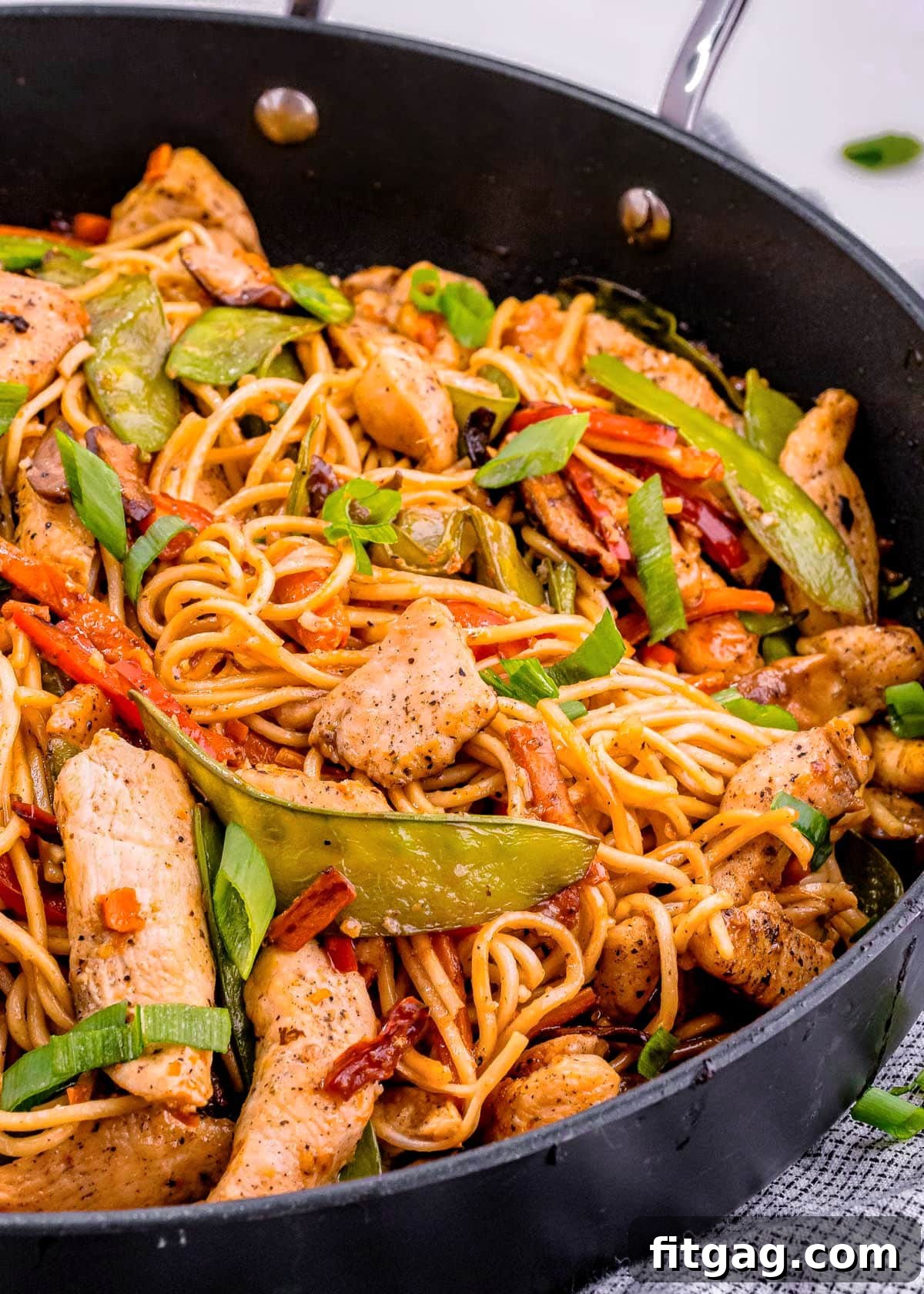 A dark skillet filled with freshly made chicken lo mein, featuring a rich mix of chicken, colorful vegetables, and noodles, perfectly sauced and ready for serving.