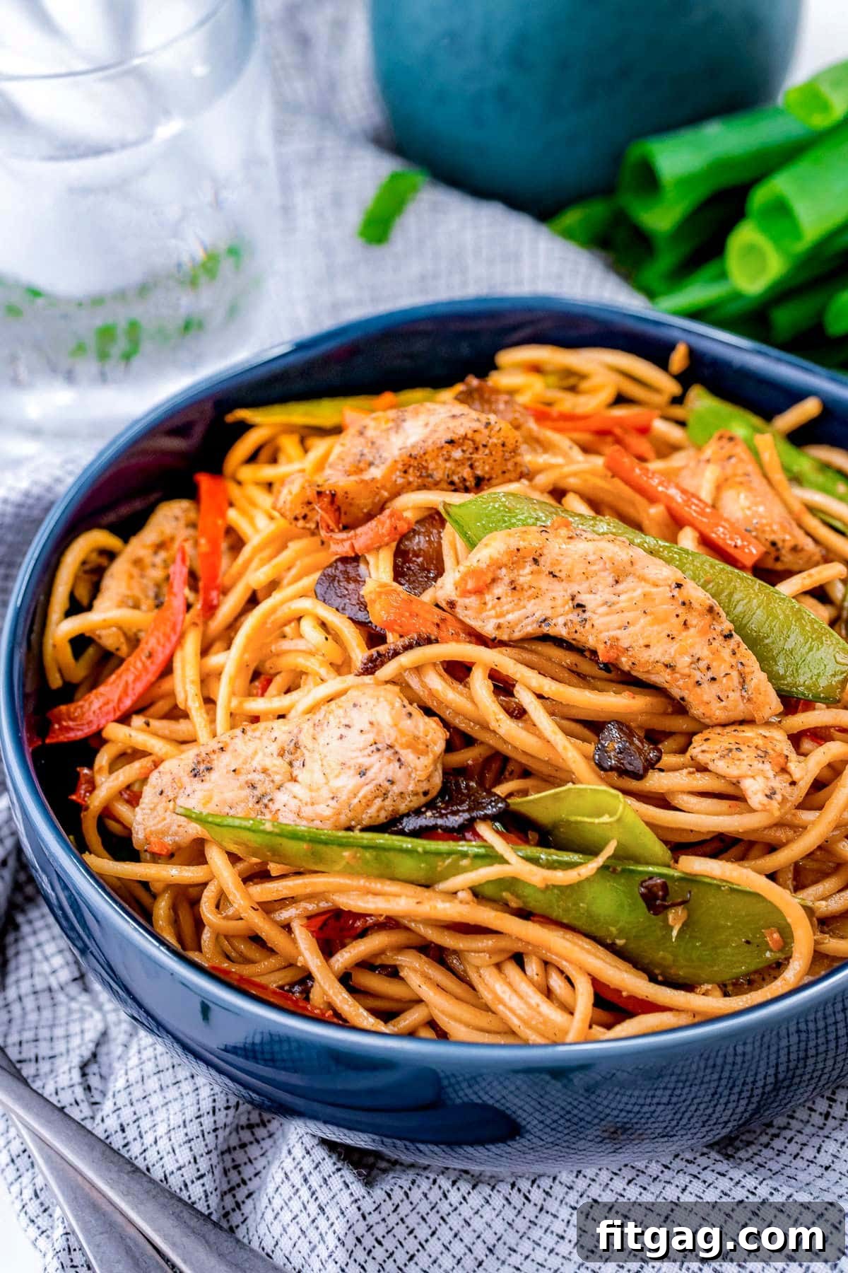 A generous serving of chicken lo mein in a vibrant blue bowl, garnished with snow peas and carrots, showcasing the rich colors and textures of the dish.