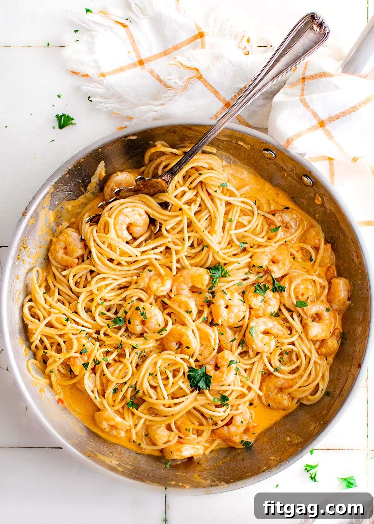 Creamy Bang Bang Shrimp Pasta 2 top down look at bang bang shrimp pasta recipe in a large skillet garnished with fresh parsley. skillet is sitting next to a white and orange kitchen towel.