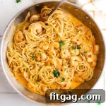 Creamy Bang Bang Shrimp Pasta 6 top down look at bang bang shrimp pasta recipe in a large skillet garnished with fresh parsley. skillet is sitting next to a white and orange kitchen towel.