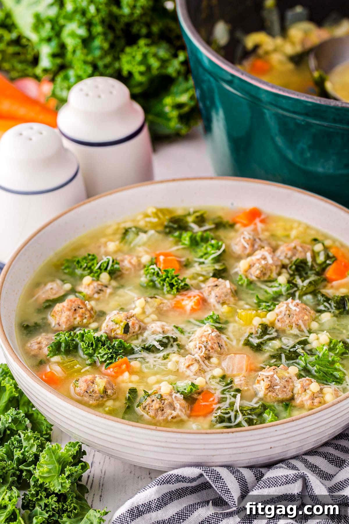 Italian Union Soup 2 large bowl filled with Italian Wedding Soup and garnished with Parmesan cheese. A dark teal dutch oven can be seen in the background. A black and white striped towel is in the front of the bowl.