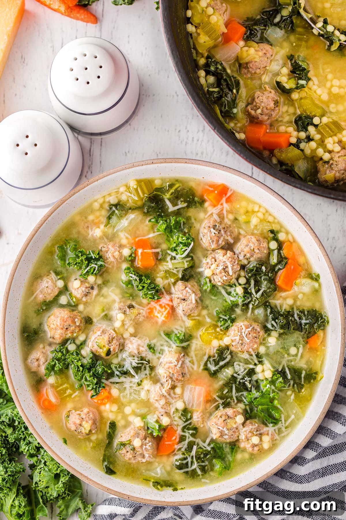 Italian Union Soup 5 top down view of bowl of italian wedding soup topped with freshly grated parmesan cheese. the pot of soup is next to it.