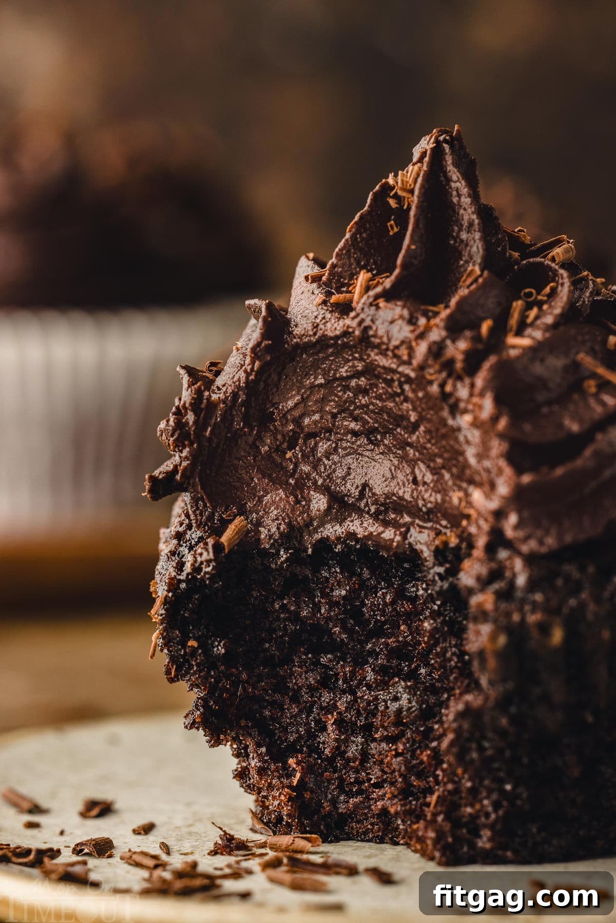 A chocolate cupcake with a bite taken out, sitting on a small plate, revealing its rich, creamy frosting piled high.