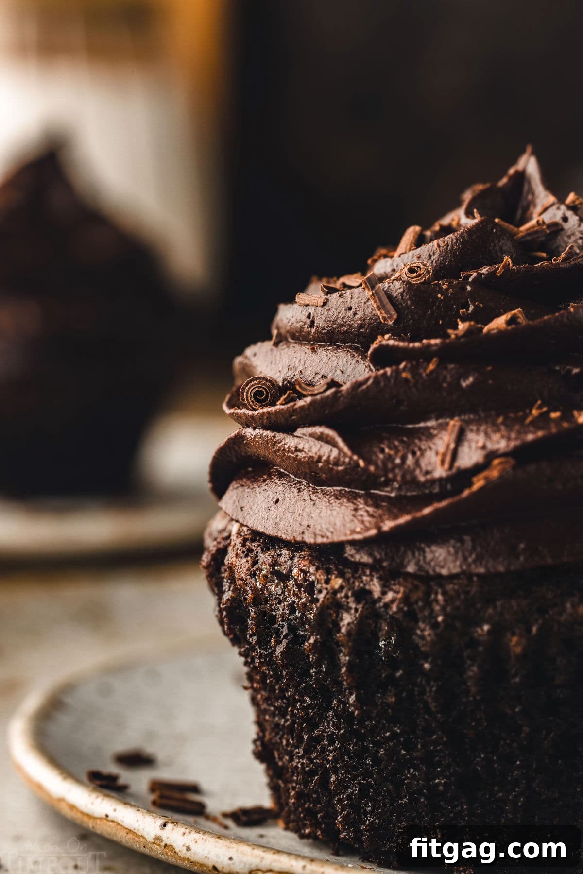Close-up view of a rich chocolate cupcake adorned with a swirl of chocolate buttercream and delicate chocolate curls, showcasing its irresistible texture.