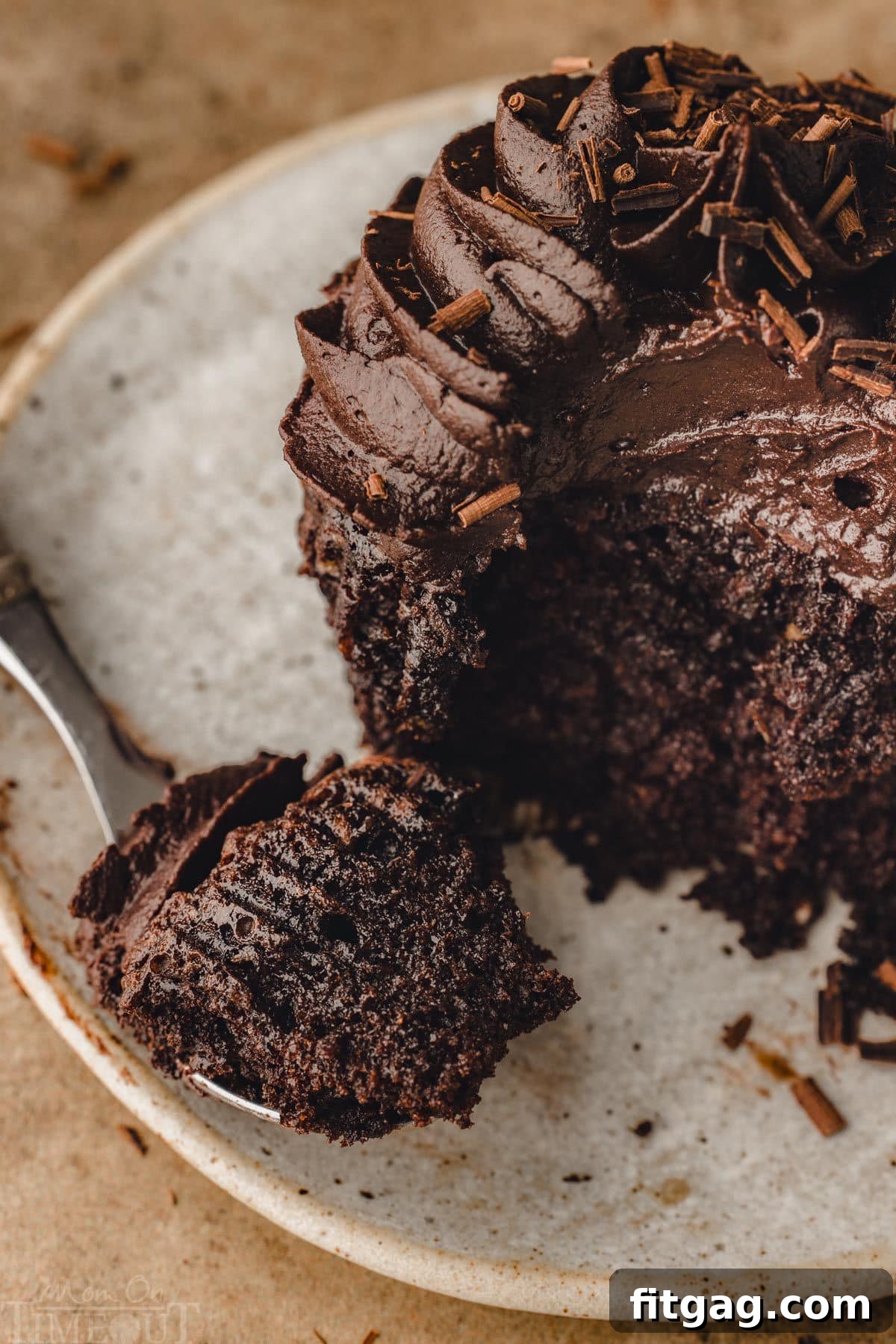 A chocolate cupcake on a small white plate with a fork nearby, showing a bite already taken from the cupcake.
