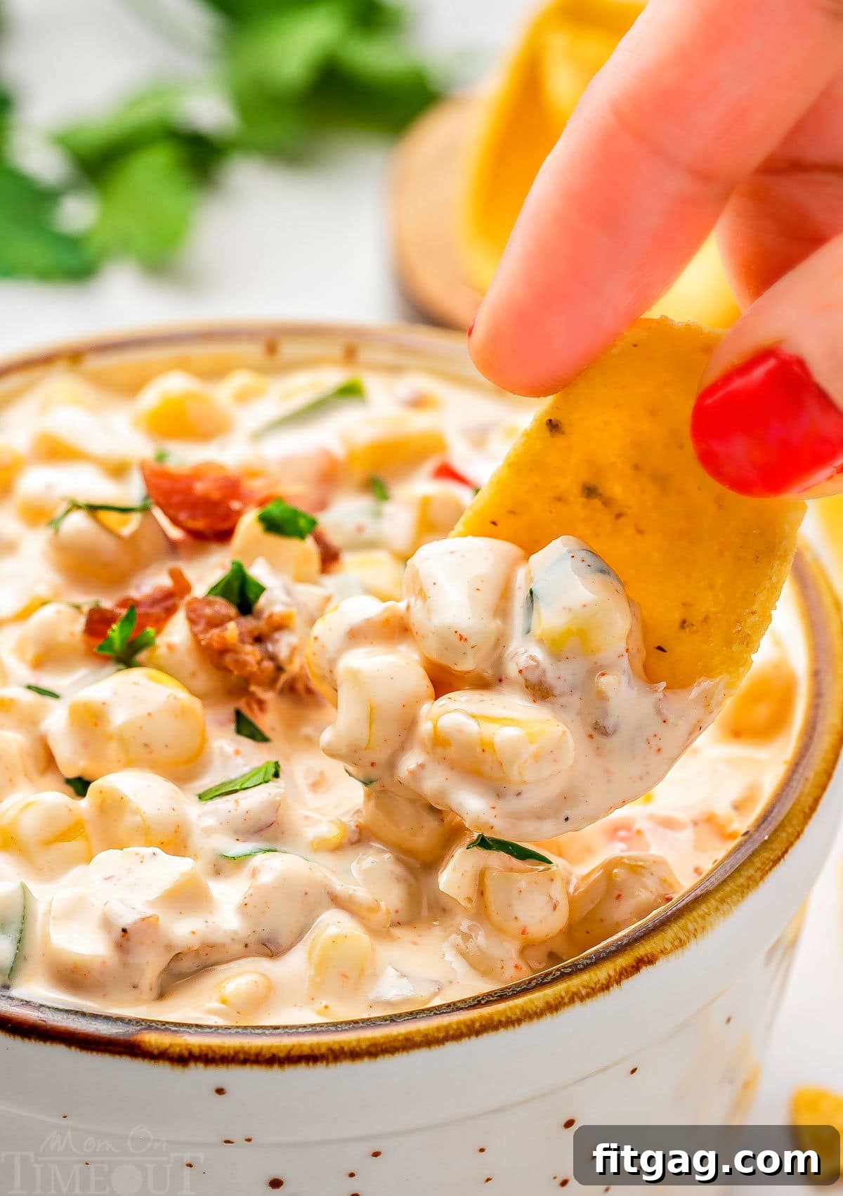Creamy Corn Delight 2 close up look at a frito scoop picking up a bit of corn dip from a small bowl. the dip has been topped with bacon and parsley.