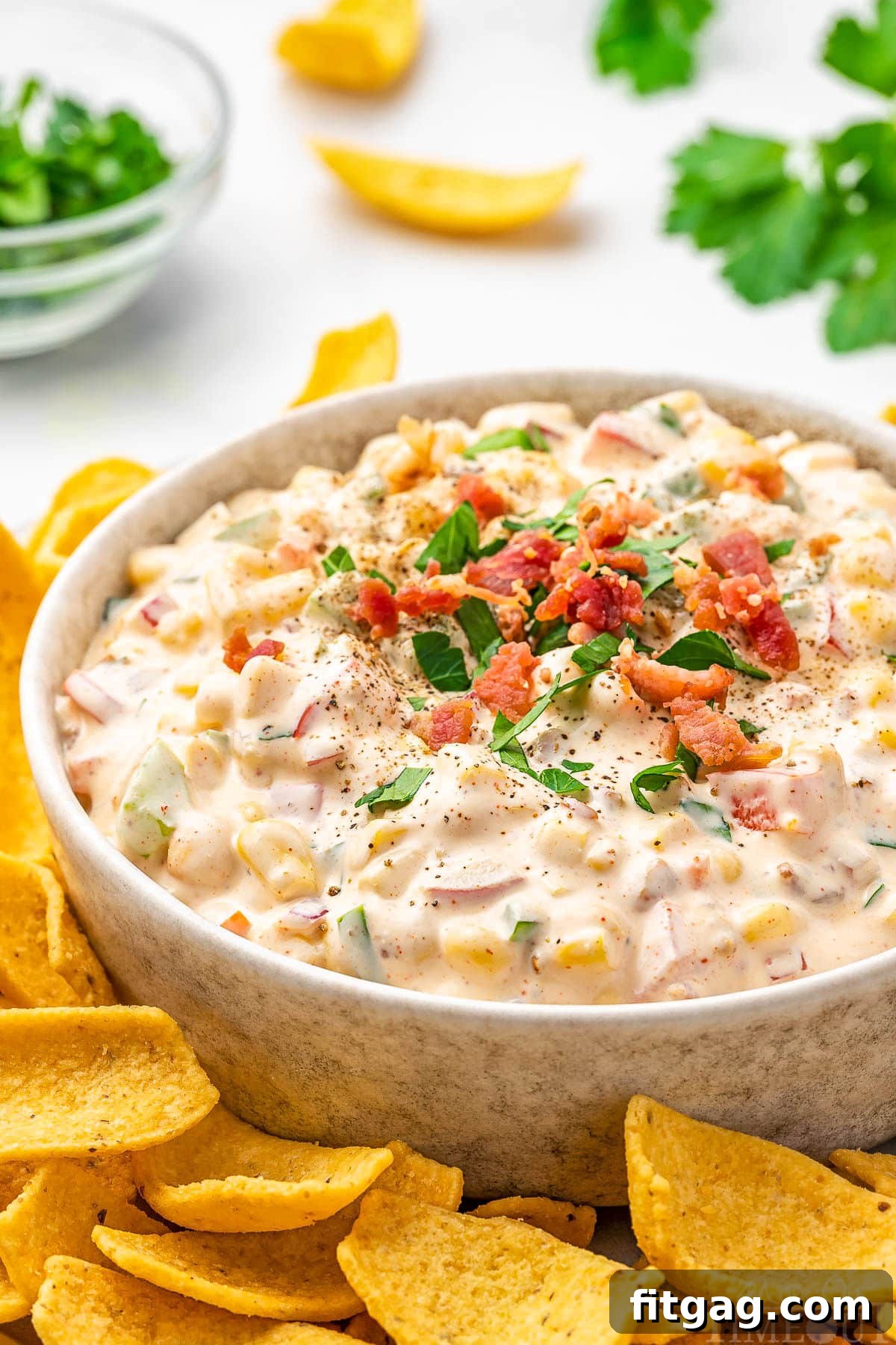 Creamy Corn Delight 3 Delicious corn dip recipe in round white bowl topped with bacon bits in parsley surround by fritos scoops ready to be enjoyed.