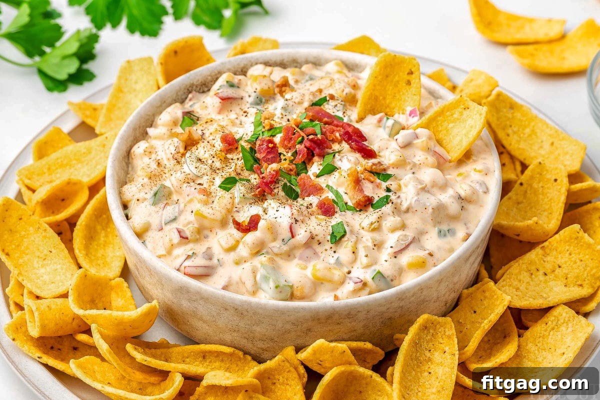 Creamy Corn Delight 5 big bowl of corn dip surrounded by fritos scoops on a platter. the dip is topped with parsley and bacon bits.