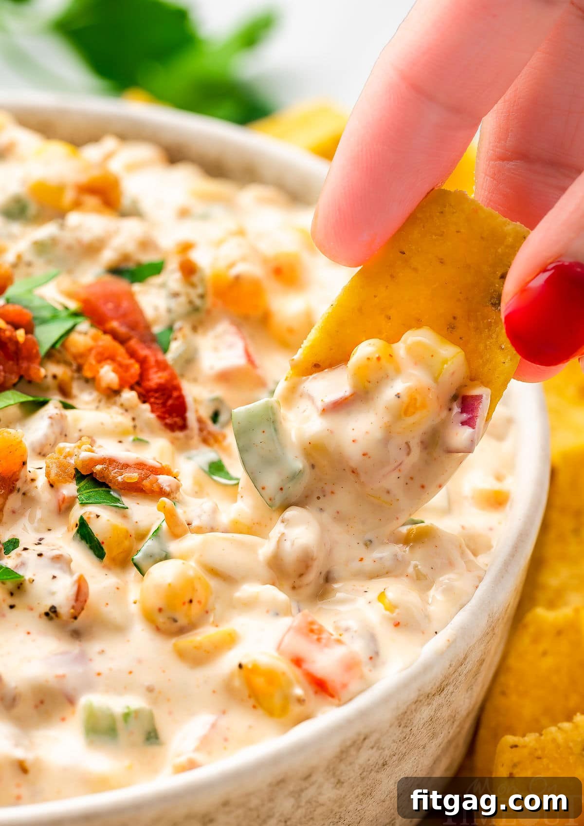 Creamy Corn Delight 6 close up look at a frito scoop picking up a bit of corn dip from a small bowl. the dip has been topped with bacon and parsley.