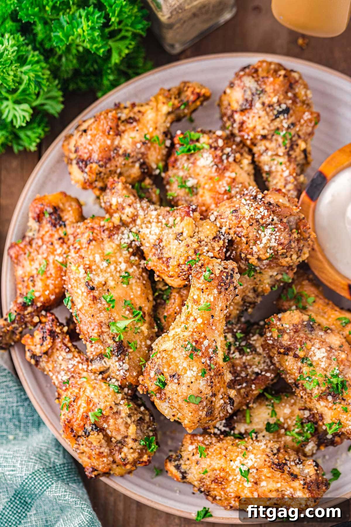 Crispy Garlic Parmesan Wings 5 A top-down view of a generously filled plate of garlic parmesan chicken wings, beautifully coated with Parmesan and garnished with freshly chopped parsley.