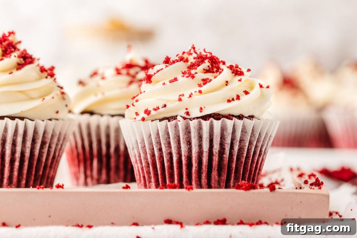 A vibrant display of red velvet cupcakes arranged on a charming pink tray, each generously frosted with creamy white cream cheese frosting and delicately sprinkled with red velvet crumbs. The scene evokes a sense of celebration and deliciousness.