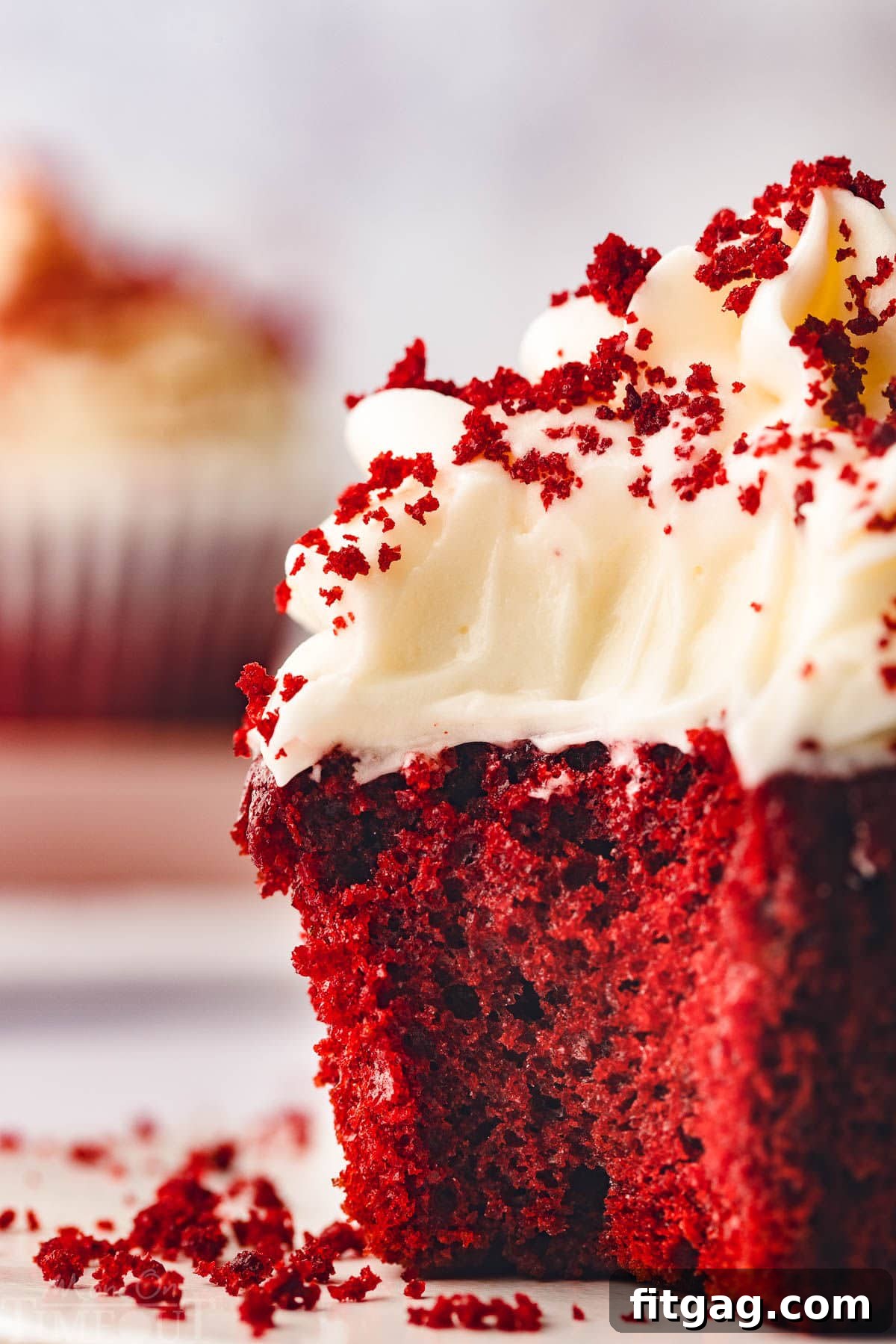 A single red velvet cupcake, artfully frosted with cream cheese frosting, positioned on a clean white surface. A bite has been taken, revealing the wonderfully vibrant red interior of the cupcake, inviting you to indulge.