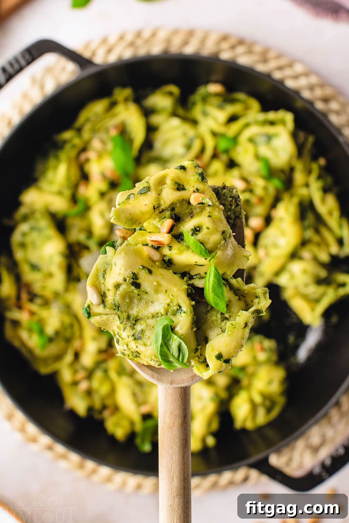 Creamy Pesto Tortellini Delight 3 spoonful of pesto tortellini held over a cast iron skillet filled with the rest of the pasta.