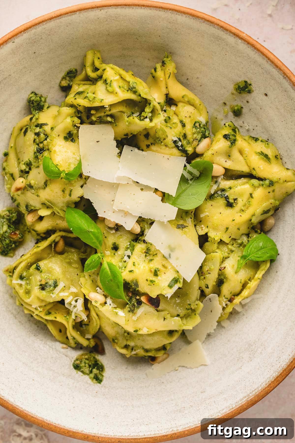 Creamy Pesto Tortellini Delight 4 top down look at a bowl of pesto tortellini topped with fresh basil leaves and Parmesan cheese.
