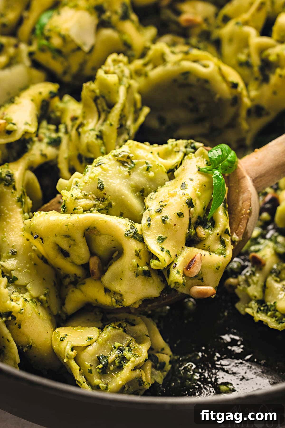 Creamy Pesto Tortellini Delight 6 wooden spoon in cast iron skillet filled with tortellini pesto.