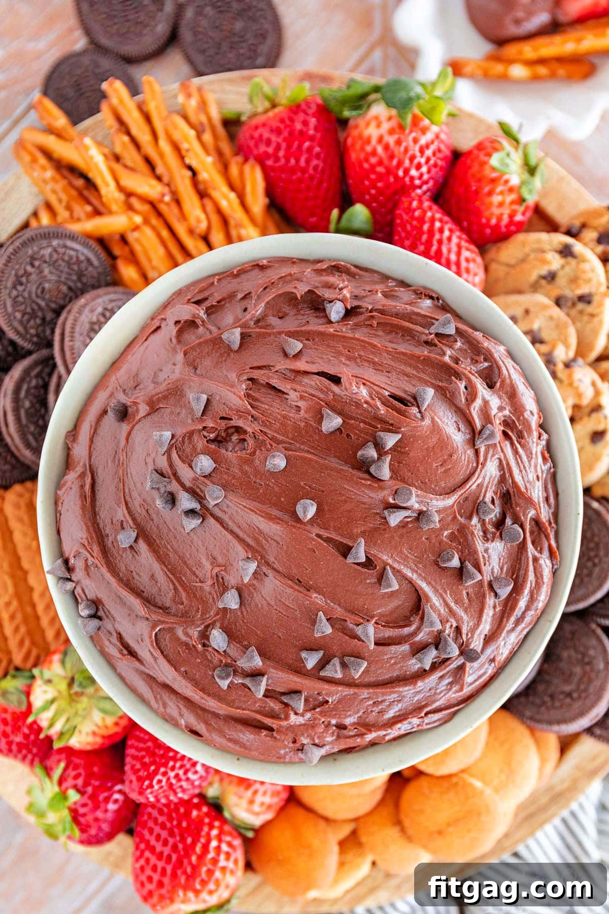 Fudgy Brownie Dip 2 Close-up, top-down shot of a bowl of decadent brownie batter dip, artfully surrounded by a vibrant selection of dippers including fresh red strawberries, sweet vanilla wafers, savory pretzels, and an assortment of cookies, perfect for a party.