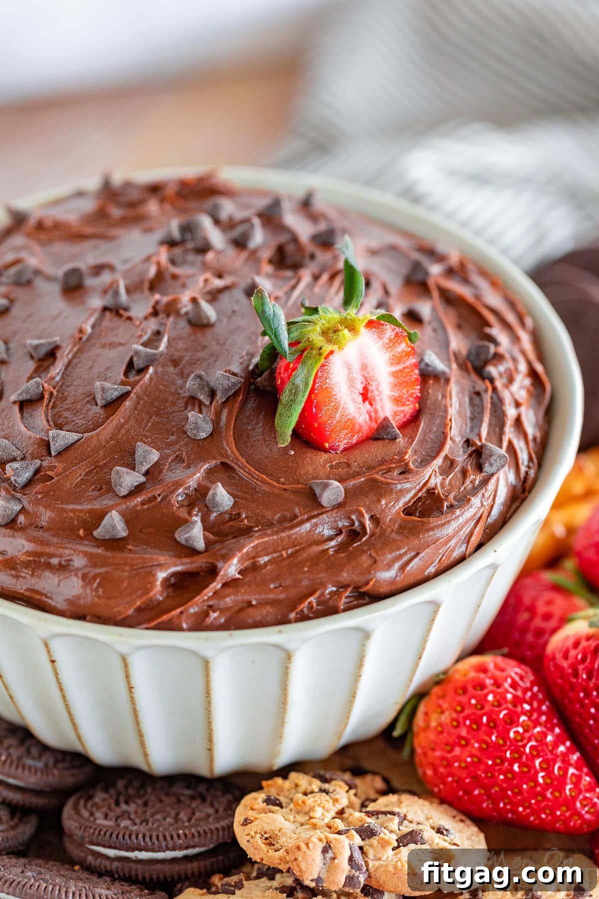 Fudgy Brownie Dip 3 A close-up view of a rich bowl of brownie dip, garnished with a vibrant half-strawberry nestled on top and a generous scattering of mini chocolate chips, highlighting its tempting texture.