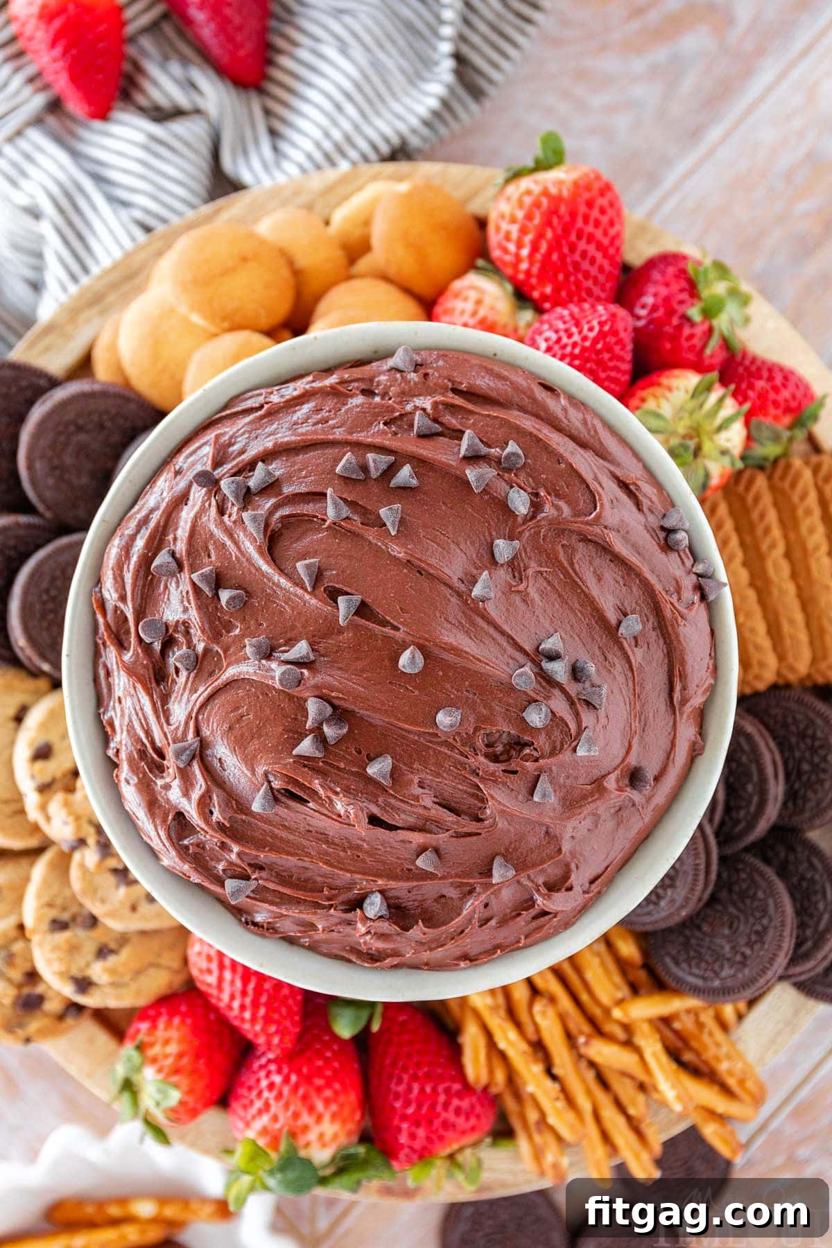 Fudgy Brownie Dip 6 Top-down shot of a bowl of rich brownie batter dip, beautifully arranged and surrounded by an enticing selection of dippers including fresh strawberries, vanilla wafers, crunchy pretzels, and assorted cookies, ready to be enjoyed.